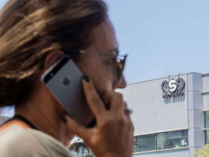 Một phụ nữ sử dụng điện thoại iPhone gần tòa nhà có văn phòng của NSO Group tại TP.Herzliya, Israel /// AFP
